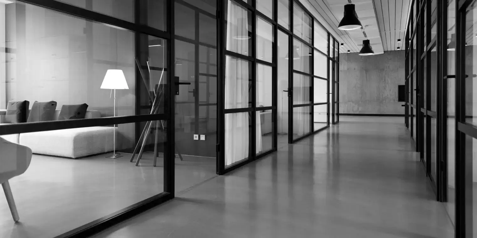 Pasillo de oficina con mamparas de cristal y luz natural, en blanco y negro