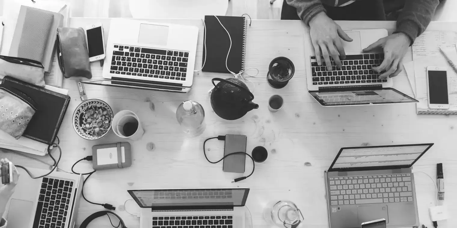 Mesa de trabajo vista desde arriba con portátiles, cuadernos y material de estudio